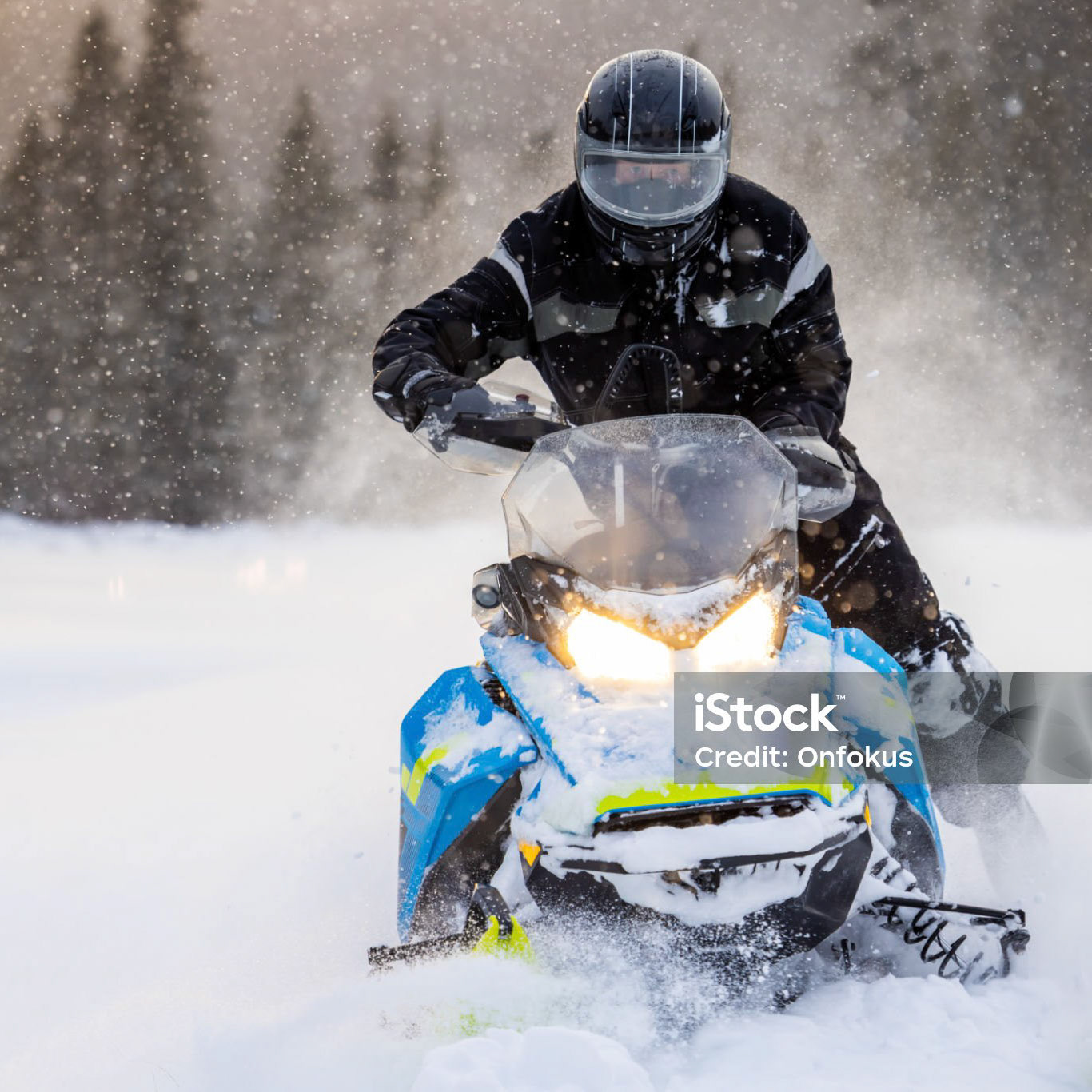 Man having fun speeding with a snowmobile through the fresh powder snow at sunset in the Laurentians Mountains, Quebec, Canada