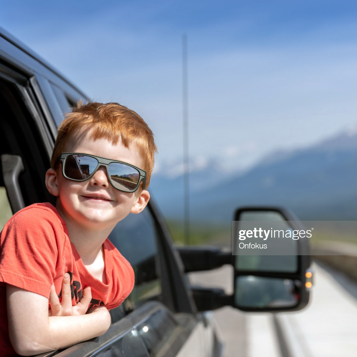 Young cute redhead child leaning on the car window and Contemplating the views while on road trip