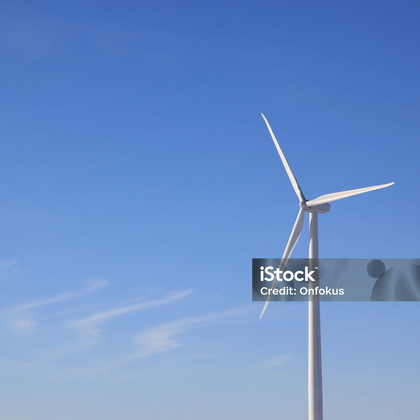 DSLR video of a wind turbine in a wind-farm generating alternative energy. There is only one wind turbine moving. The sky is clear blue with only few clouds on this winter day.