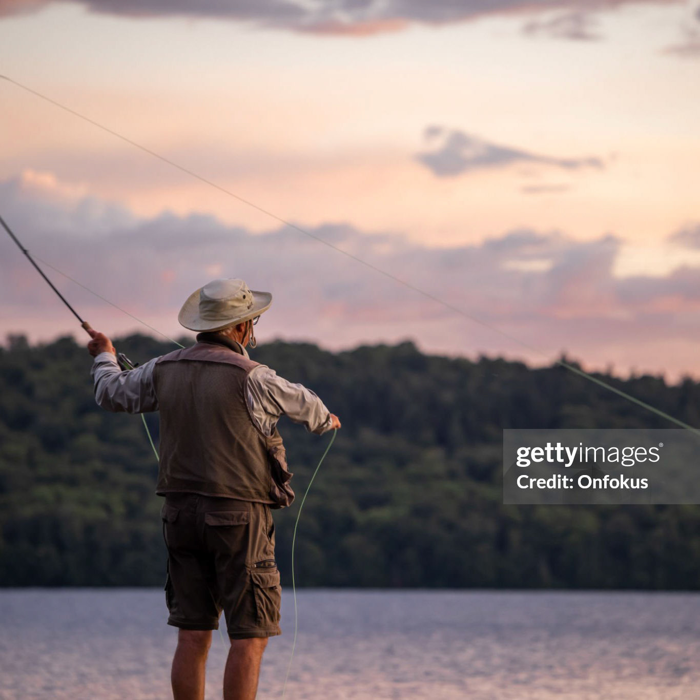 Senior Man Fly-Fishing at Sunset at the lake. He is standing on a pier at Lac St-Joseph, Quebec, Canada.