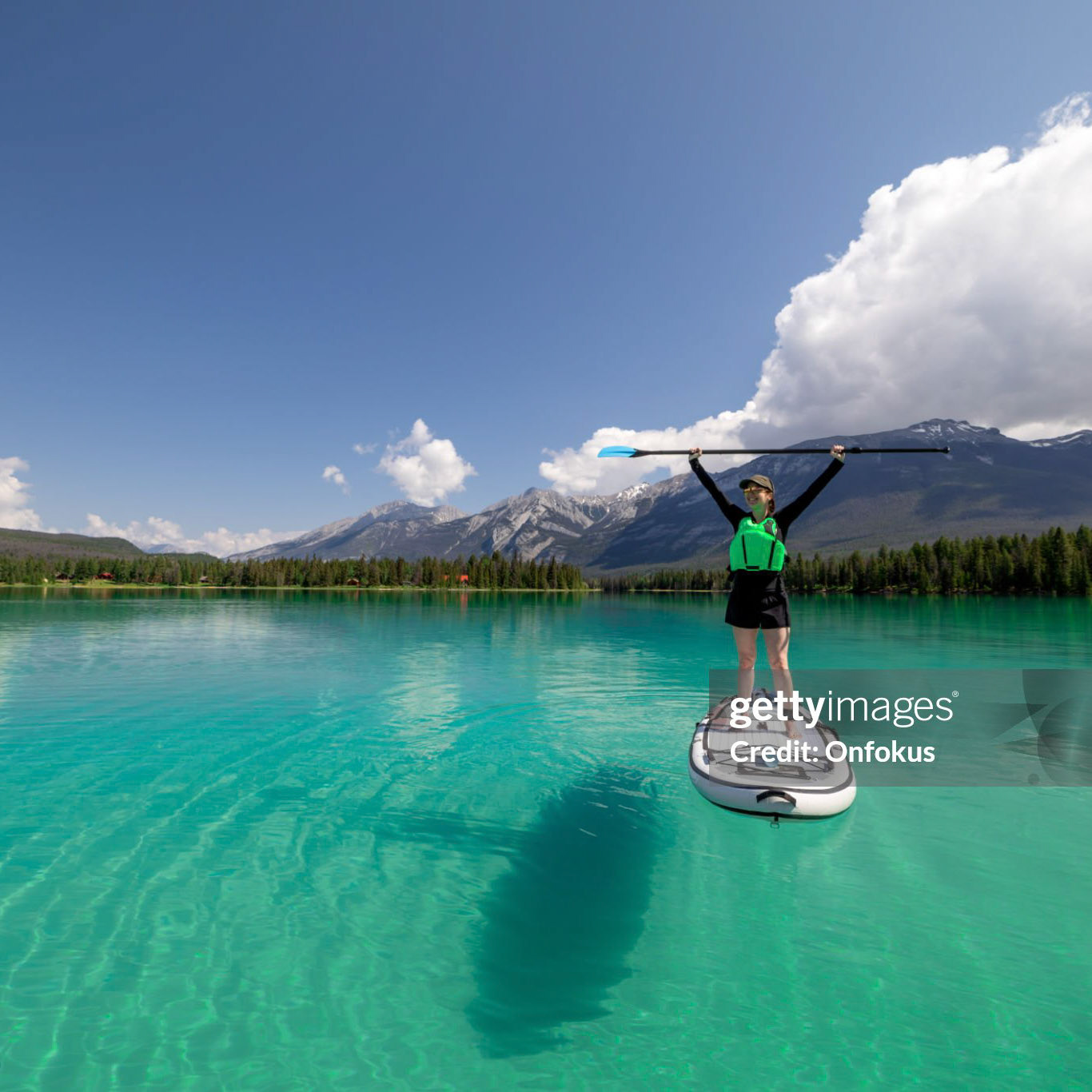 A woman is paddleboarding on Edith Lake in Jasper National Park, Alberta. The turquoise colored lake is very calm. Its is a beautiful sunny summer day in the Canadian Rockies.