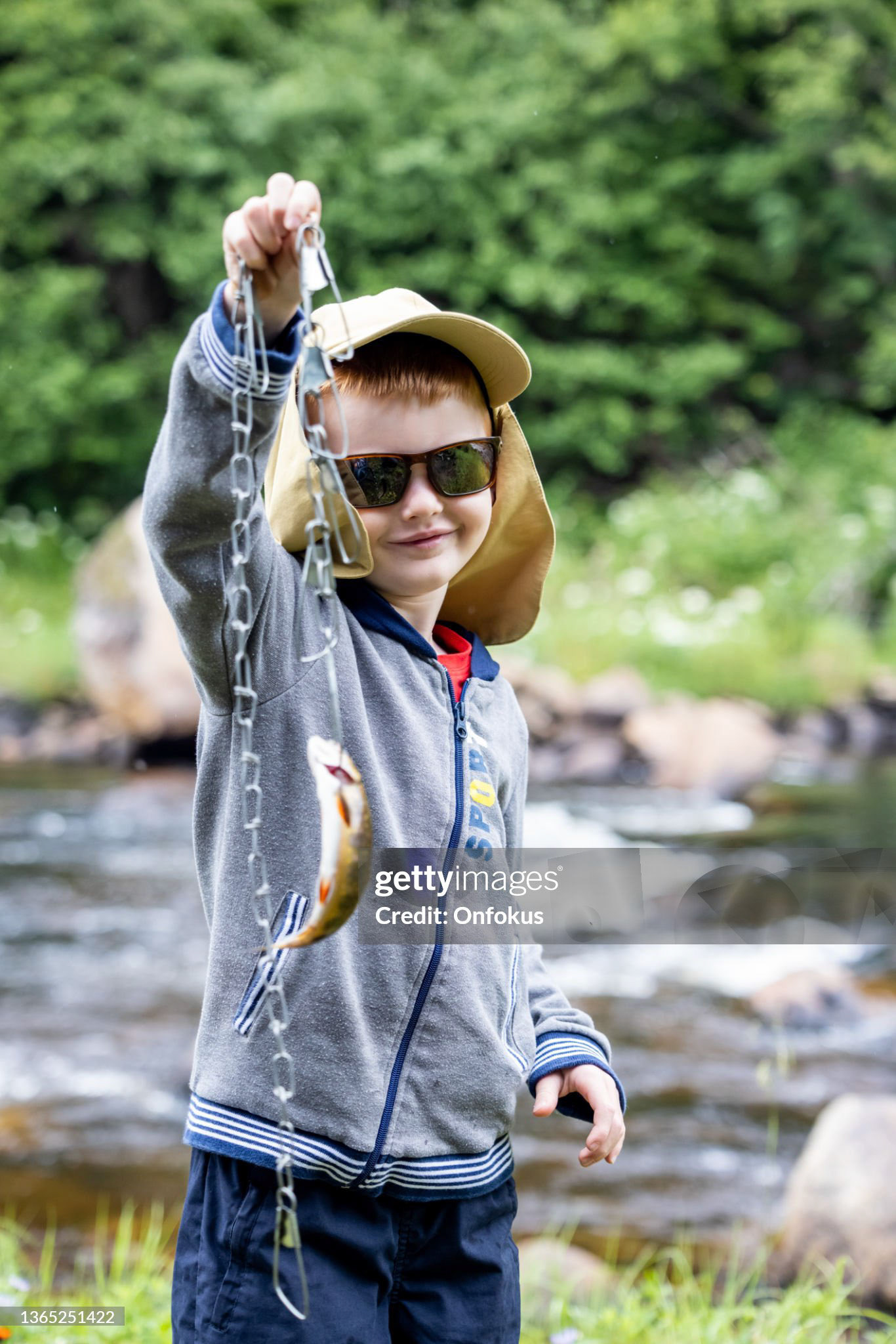 Cute Redhead Boy Fishing in the River in Quebec and Showing the Catch of the day, a trout. He is looking at the camera and smiling.