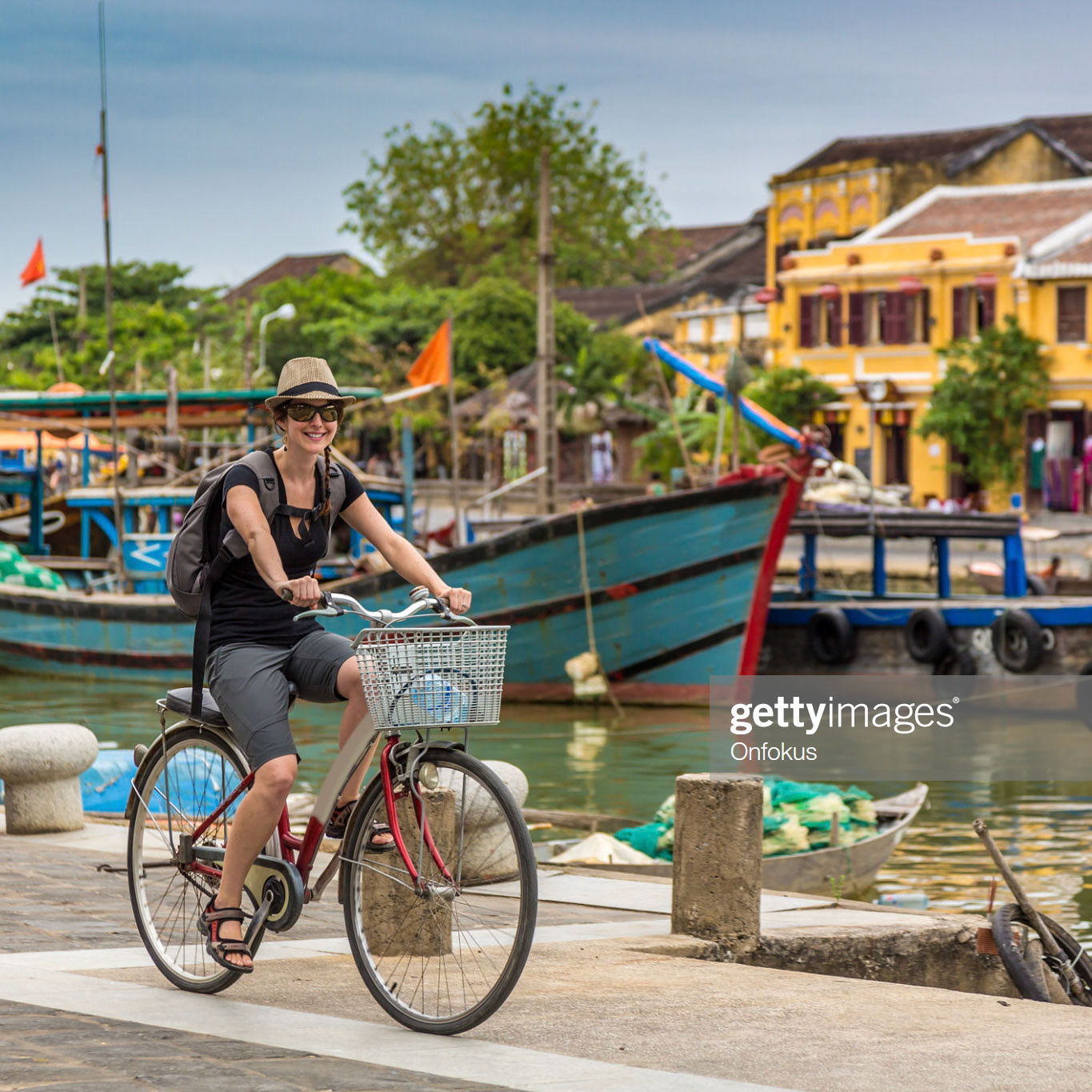 Woman Tourist Cycling in Hoi An City, Vietnam. She is happy and smiling and the coloured buildings of the city are in the background.