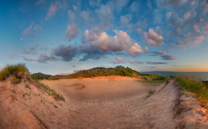 The sun's rays touch the tops of the dunes at Pyramid Point as the moon sets.