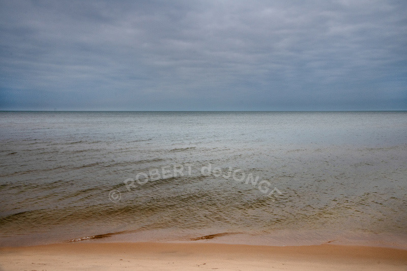 A light breeze creates cat paws on the water and and small breakers on the beach. Absent — The Lake Tree