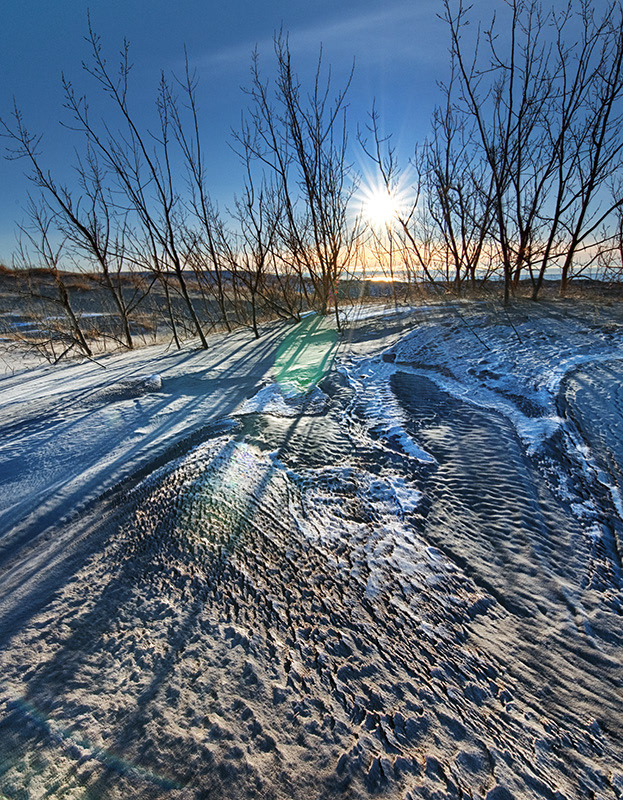 Deeply textured landscape of the dunes made by snow, ice, sand, and wind, and lit by the setting sun.