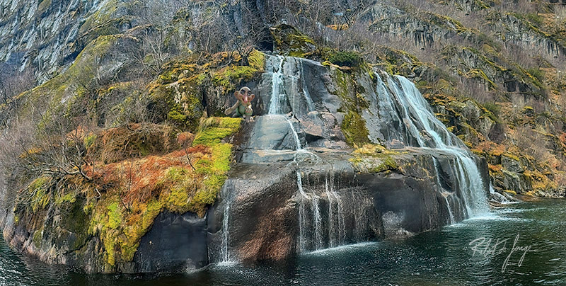A waterfall cascades over a mossy ledge in the Trollfjord, Norway