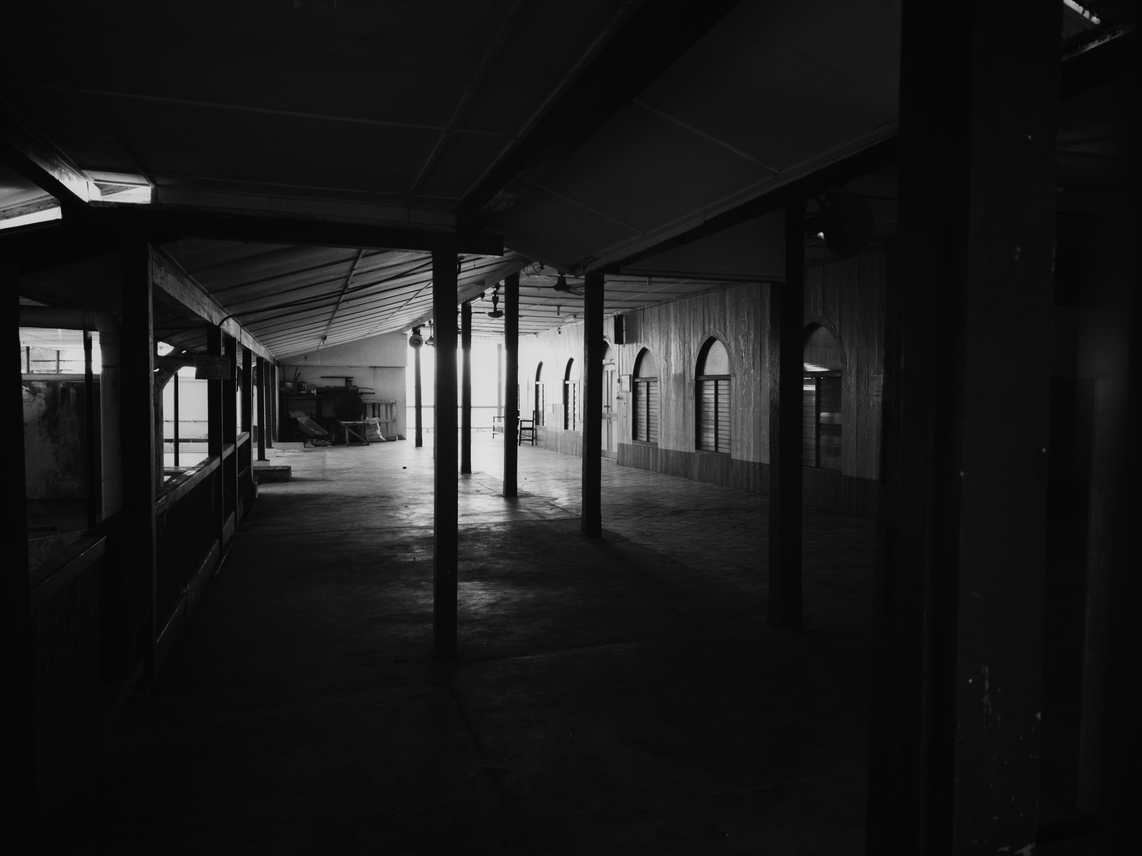 Dark black-and-white interior of a dis-used mosque at Lorong Sempit, Kuching, with empty corridors, arched windows, pillars and strong shadows creating a quiet abandoned atmosphere.