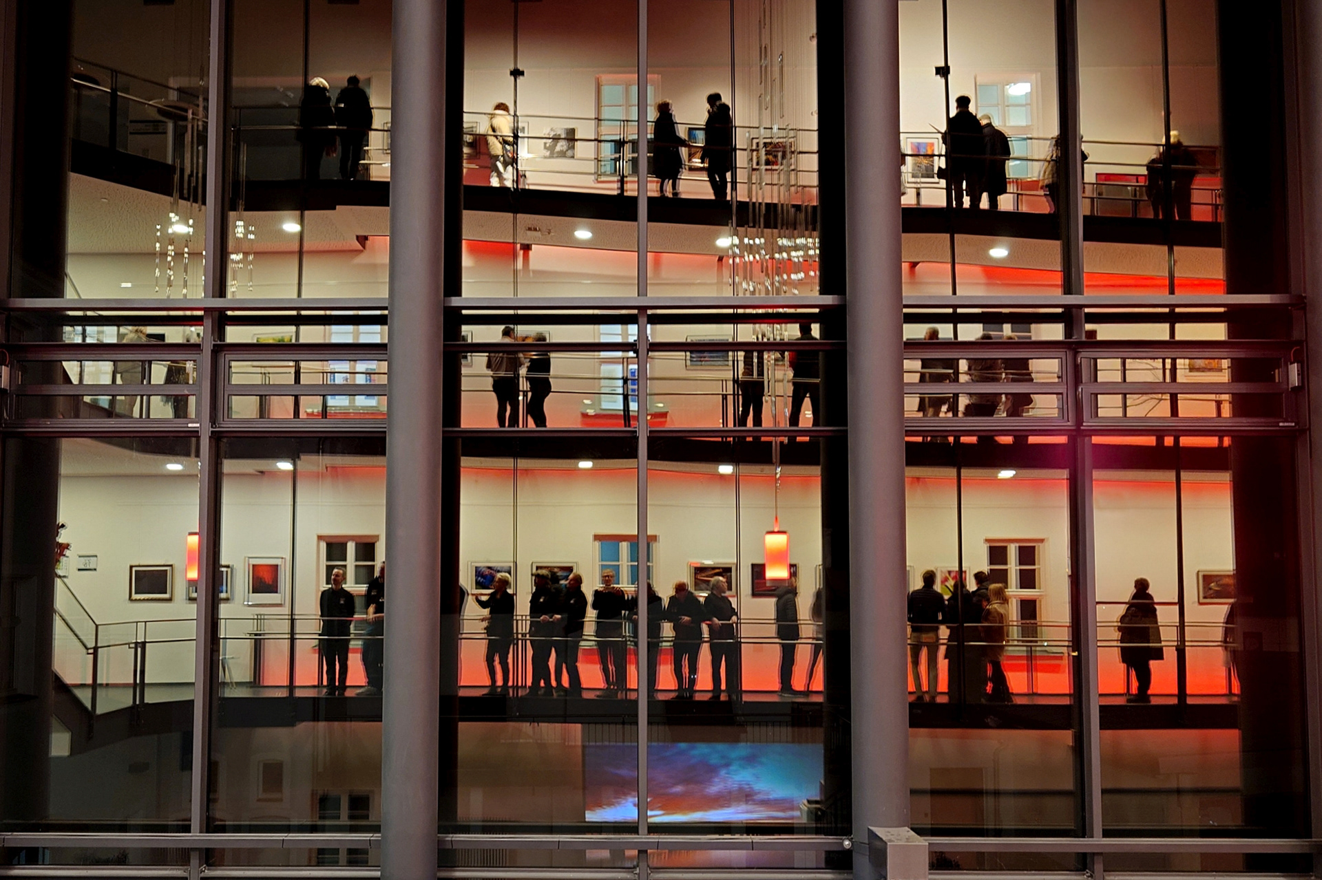 Vernissage-Besucher und Teilnehmende einer Ausstellung der Fränkischen Lichtmaler spiegeln sich in der gegenüberliegenden Fensterfront