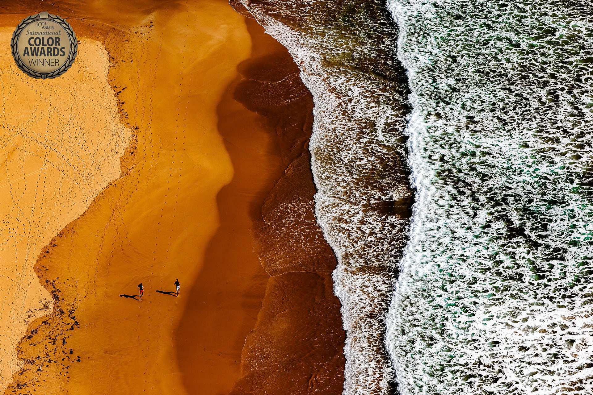 "Runners" - Enroute from Antalya to Alanya over the Mediterranean coastline I saw two men jogging on a sandy patch of beach. I was almost directly above them. I had only a few seconds to compose the frame with my telephoto zoom lens before I passed the runners and the part of the beach that had a total of six tonal shades and textures. The result is this award winning photograph.