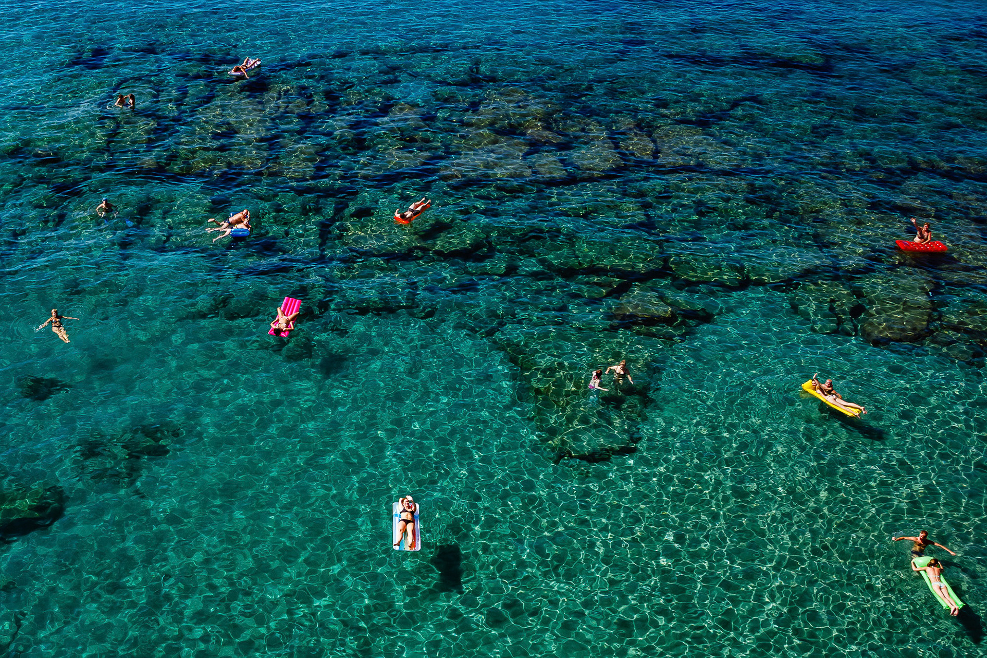 "Floats" - Tourists lazily sunbathing on their floats with comfortable personal spaces around them in crystal clear Mediterranean water form this serene image where the viewer's eyes move around "connecting the dots".