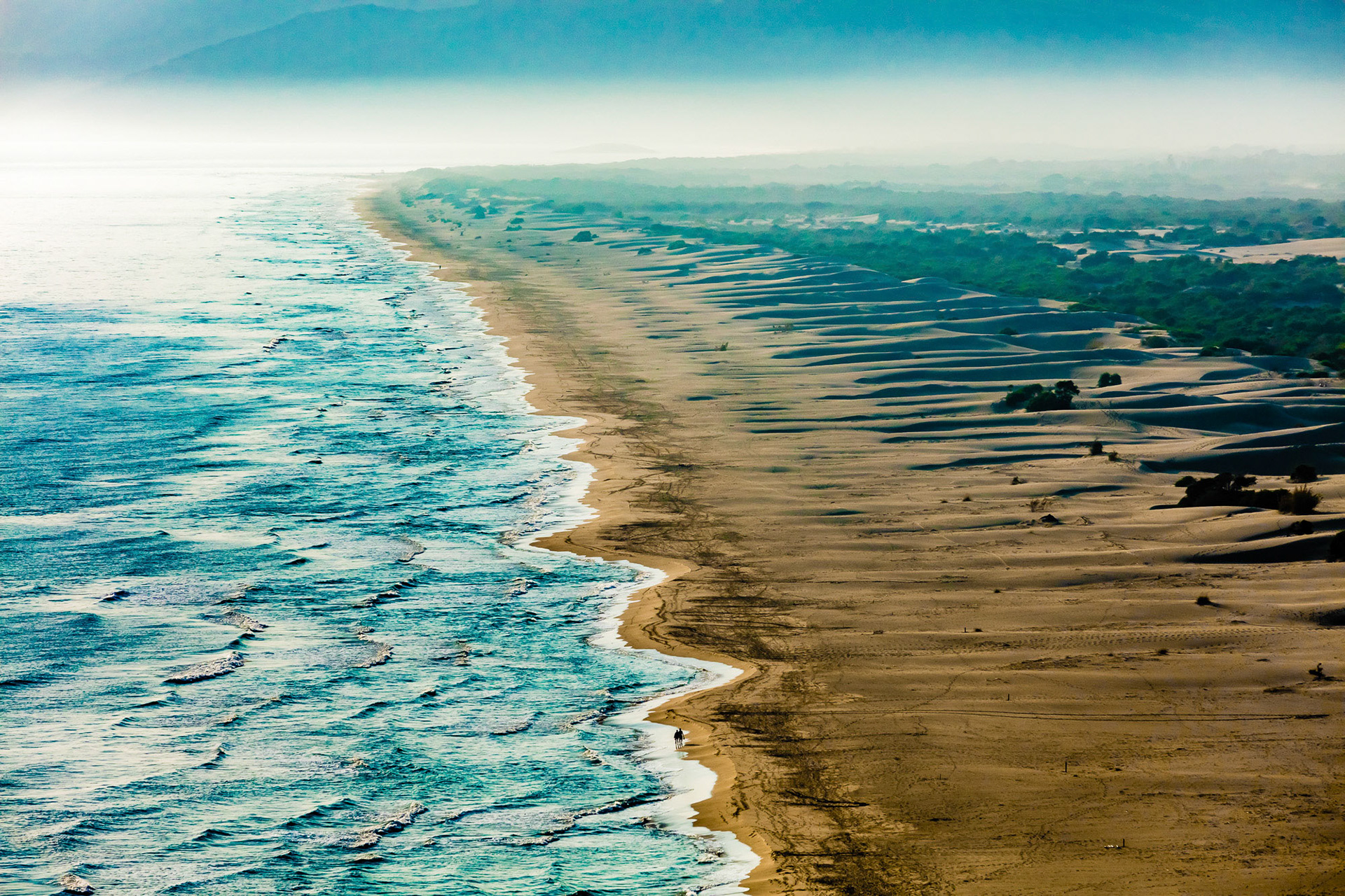 "Ripple" - I felt that the best way to show the size of this ten mile beach with its sand dunes and foliage was to fly high and compress it with my telephoto lens. The resulting ripples on the sea and the sand gave this image its name. The tiny couple in the foreground and the person way back help us see the scale of this immense natural beach where sea turtles regularly nest.
