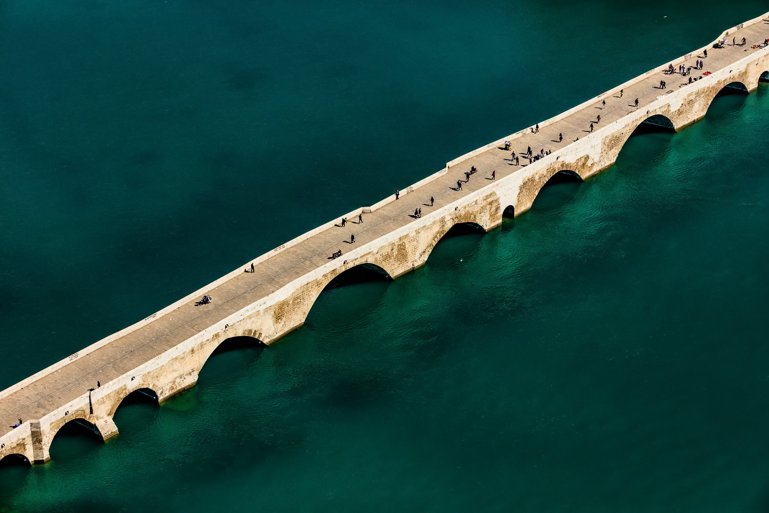 "Stone Bridge" - Stone Bridge (Taşköprü) is a Roman monument that connects the east and west sides of Adana city center on the Seyhan River. During my childhood years, we passed through Taşköprü almost every day in the summer on our way to the sea in Karataş. The bridge, now closed to vehicle traffic, is the most important symbol of Adana for me. I had to shoot it in a different and impressive style. I isolated the bridge inside the blue green shades of the Seyhan River. The people on it added extra color and richness.