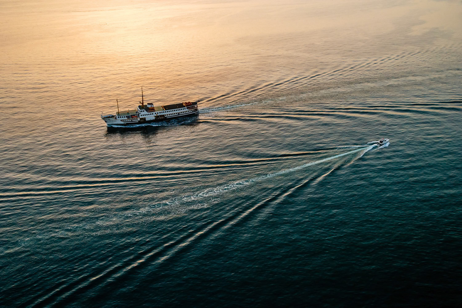 "Backwash" - I captured this image of a ferry boat and a small day boat as they pass by, while flying along the Marmara Sea. The setting sun's backlight bring out the wake in the water and give the image a teal and orange look.