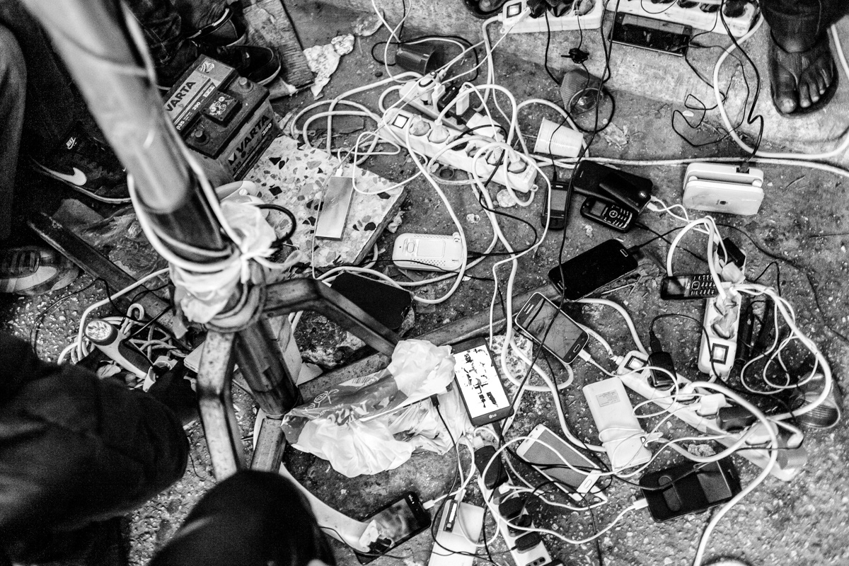 Refugees and migrants from Gambia and Senegal, charging their phones in one of the tent in camp. During the period of harvesting local residents share and allow people from the camp to connect to electricity and water. Immediately after the end of the olive season in December, local police and carabinieri officers show up to cut off the electricity.