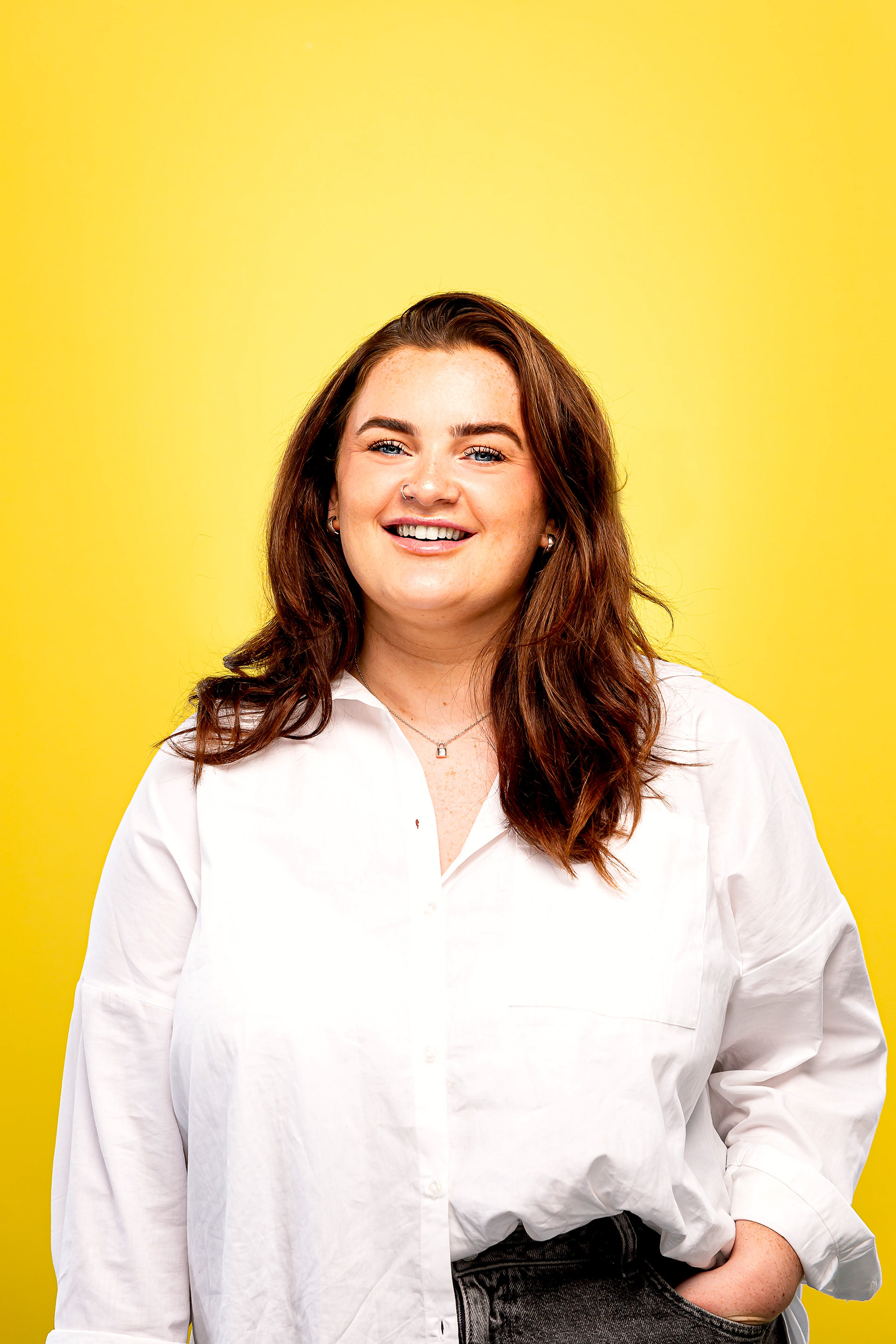 Portrait of a brunette woman in smart caual cothing with a bright yellow background