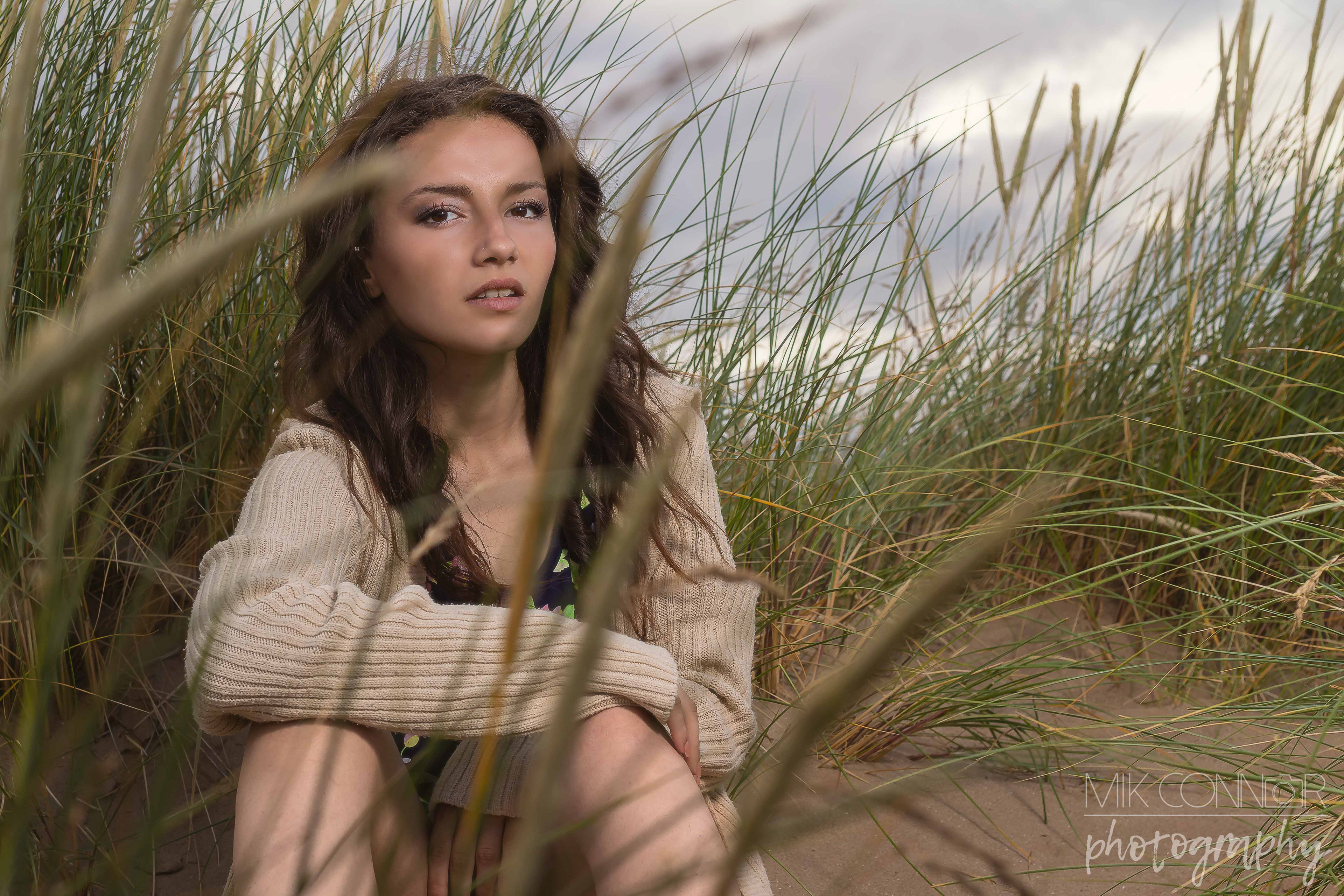 Portrait of a woman sat on a sand dune surrounded by sea grass
