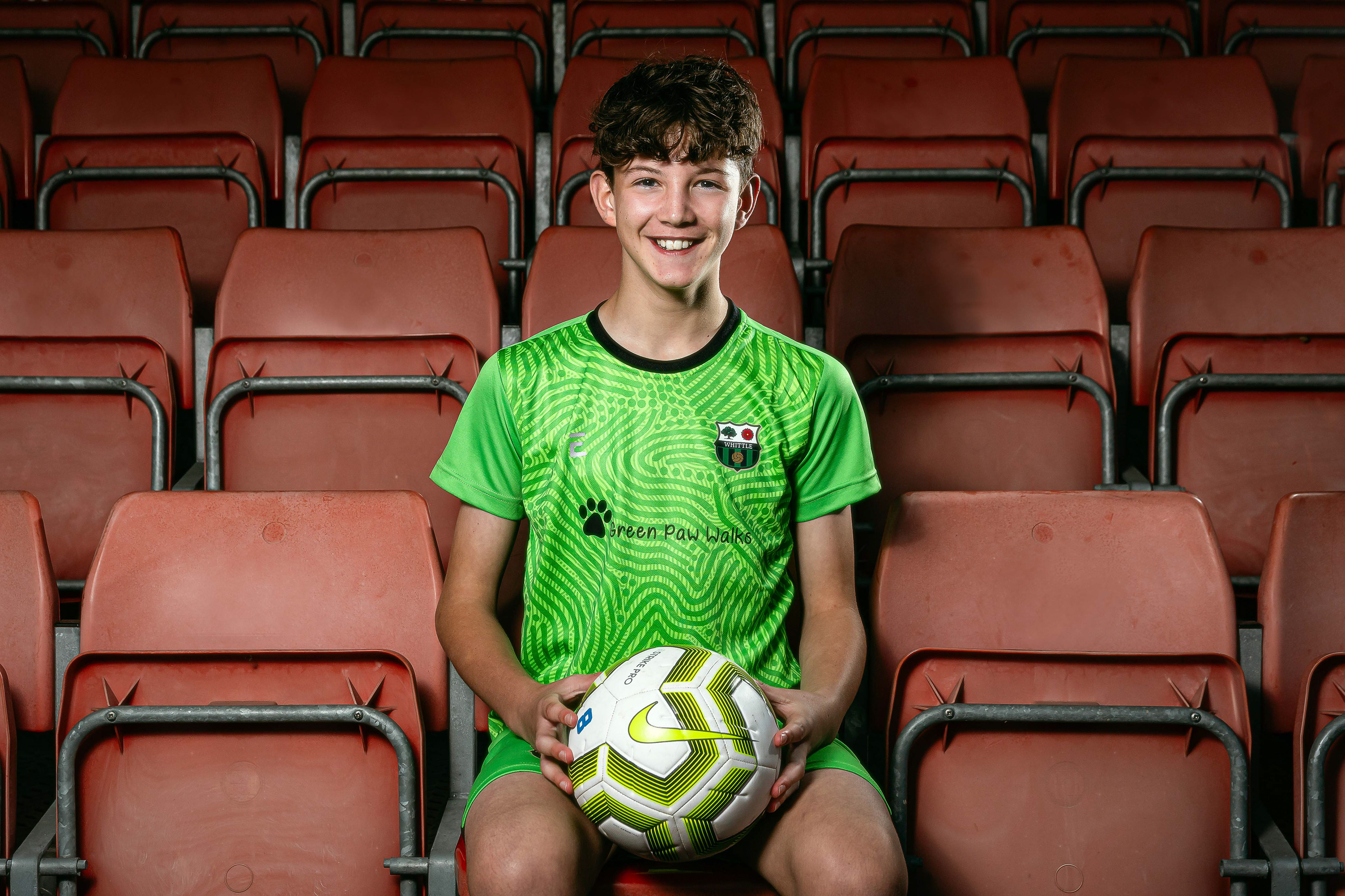 Portrait of a young male footballer sat in an empty stand showing off his team's kit