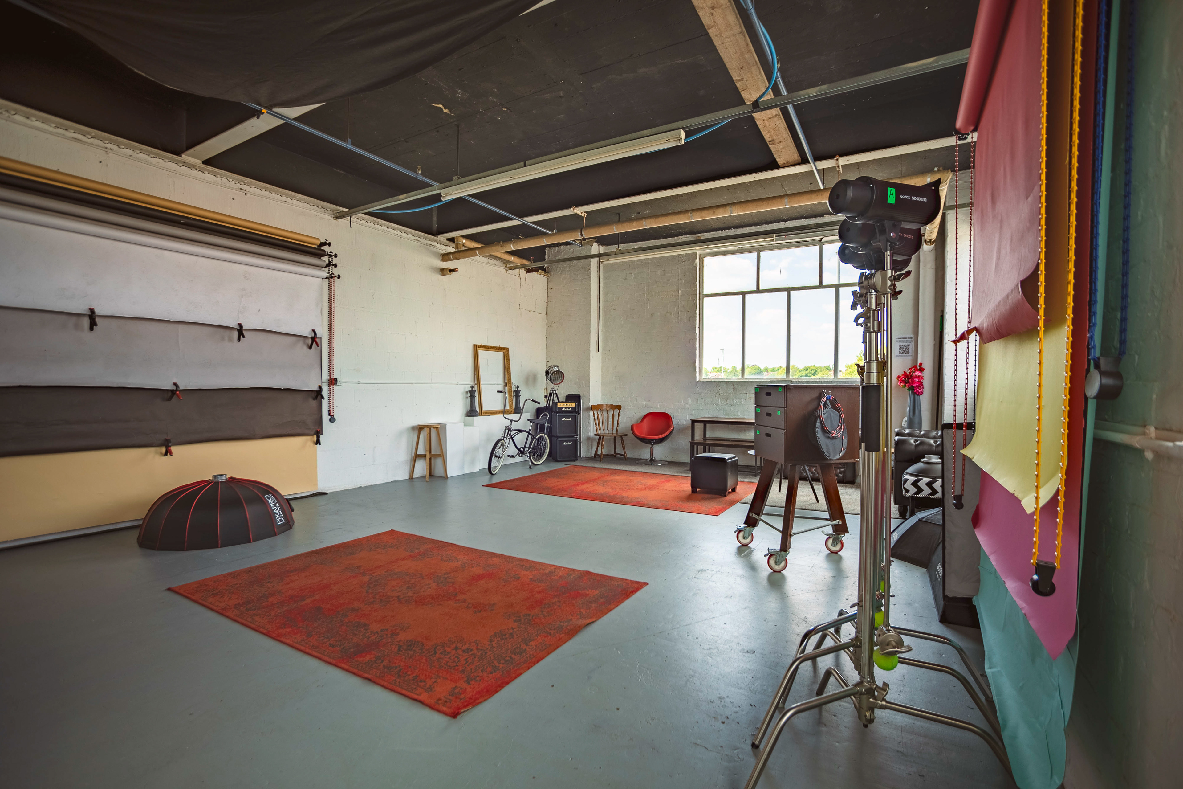 View of a photography studio showing a big window, a variety of backdrops lights and furniture props