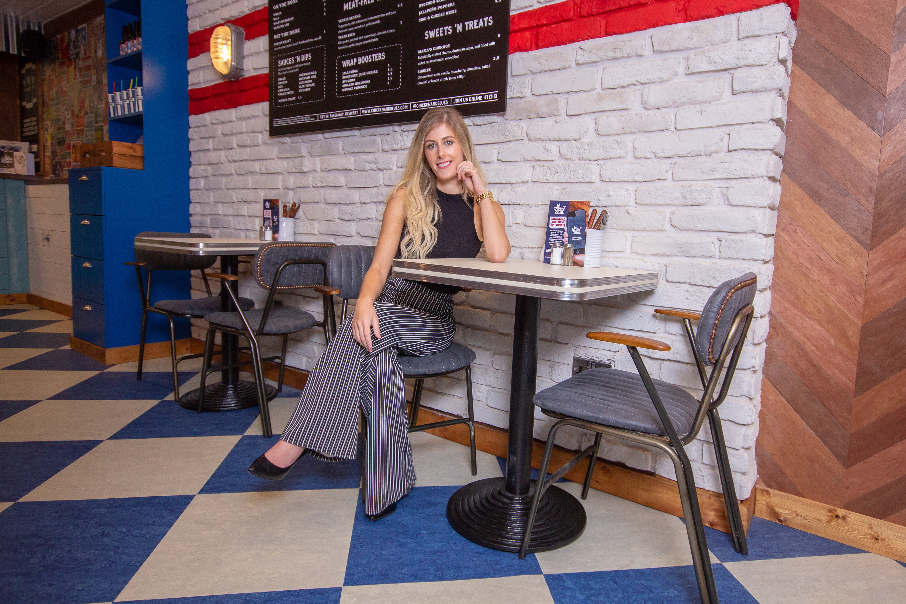 KTM Designs seated at a retro table in the Chicken & Blues dining area with a checkerboard floor. 