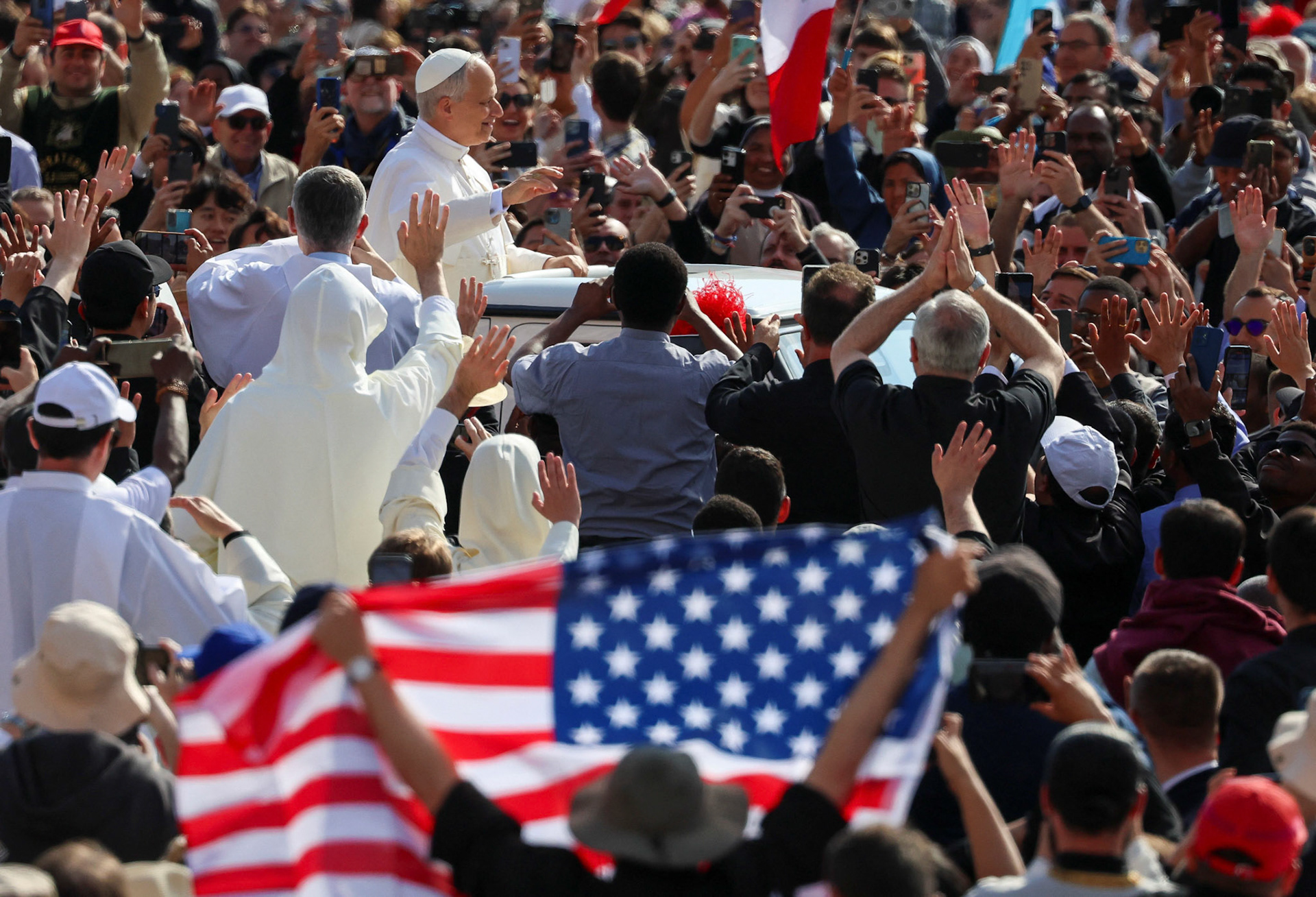 An American flag is displayed as Pope Leo XIV, formerly Cardinal Robert Francis Prevost, waves as he arrives to celebrate his inauguration Mass at the Vatican May 18, 2025. He is the first American pope in history. (OSV News photo/Claudia Greco, Reuters)