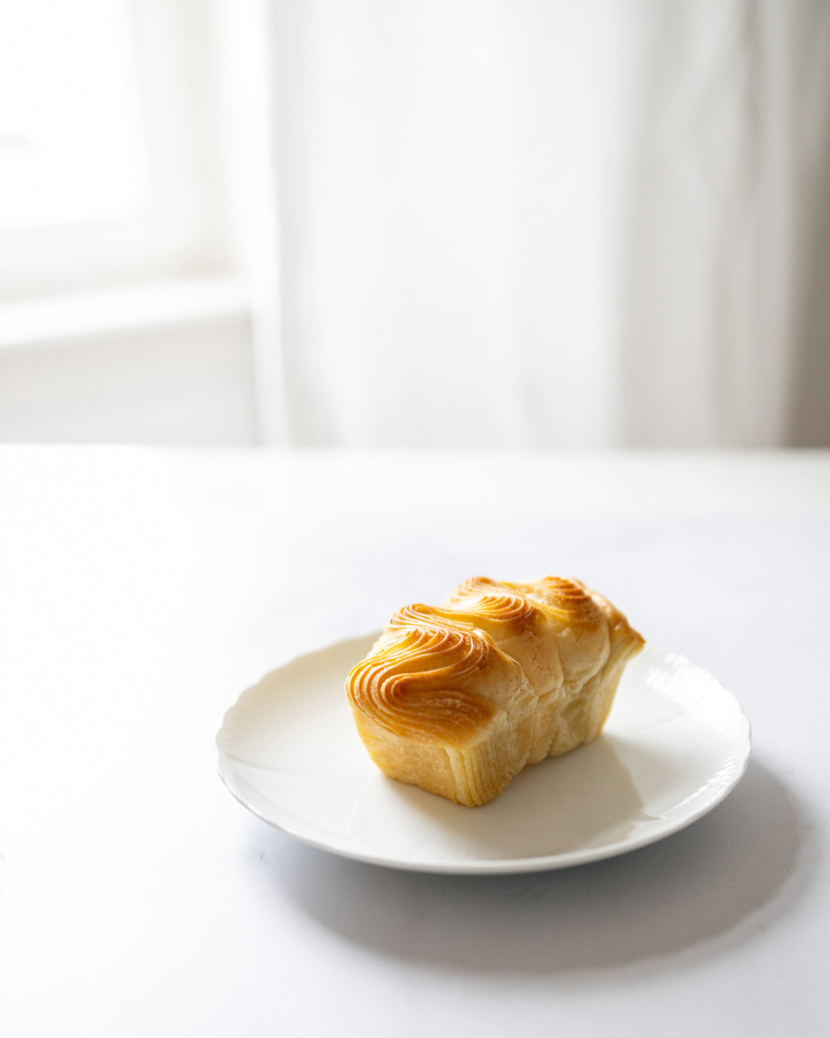 Brioche on a white plate against a white curtain.