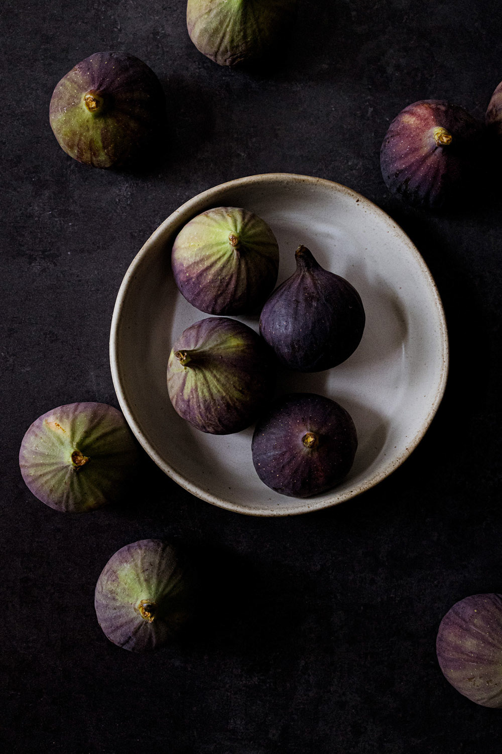 Figs scattered on a table and bowl seen from above.