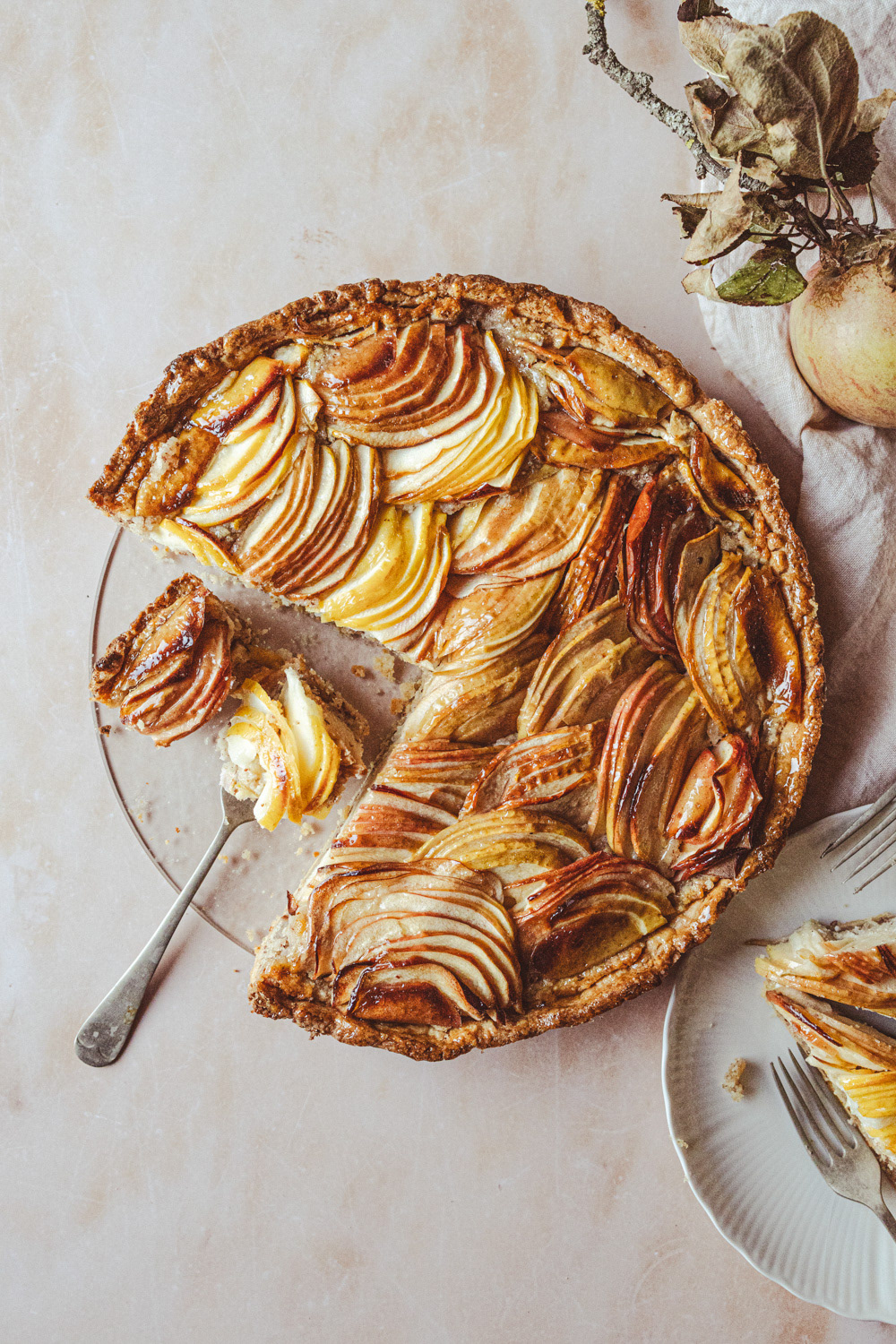 Top view of apple tart with several pieces cut off. Fork with a piece of apple tart and plate can be seen.