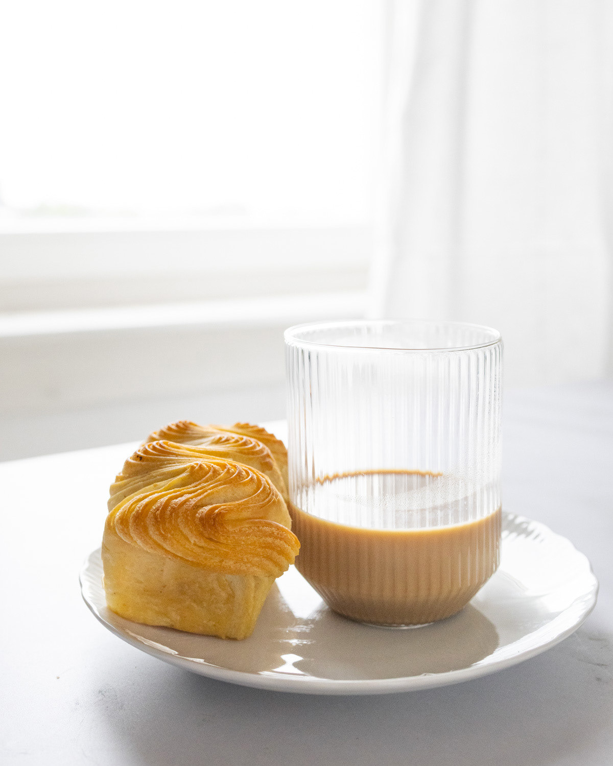 Front view of brioche and glass of oat milk on a white porcelain plate.