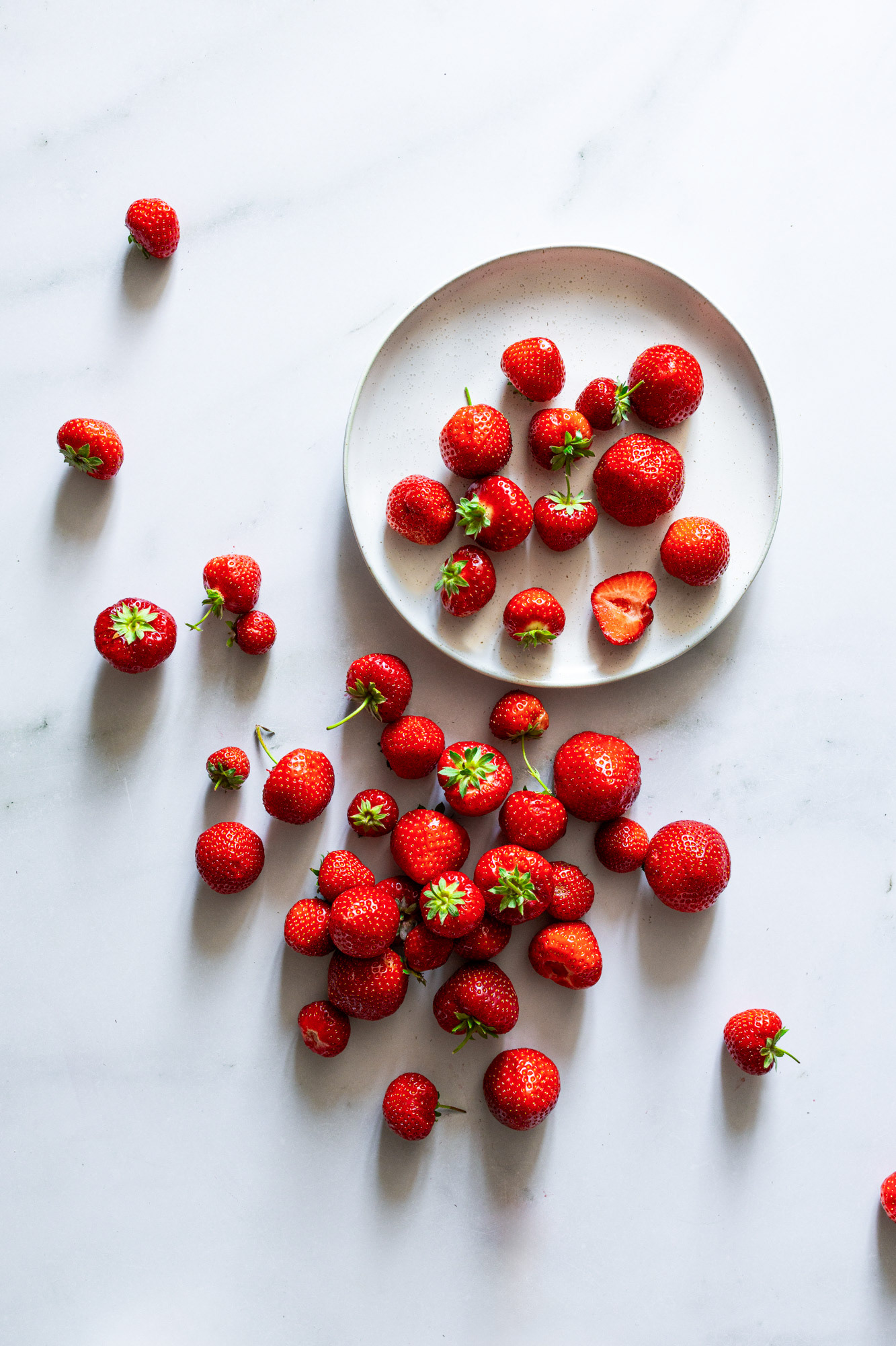 Red, ripe, delicious strawberries on plate and on marble table surface.