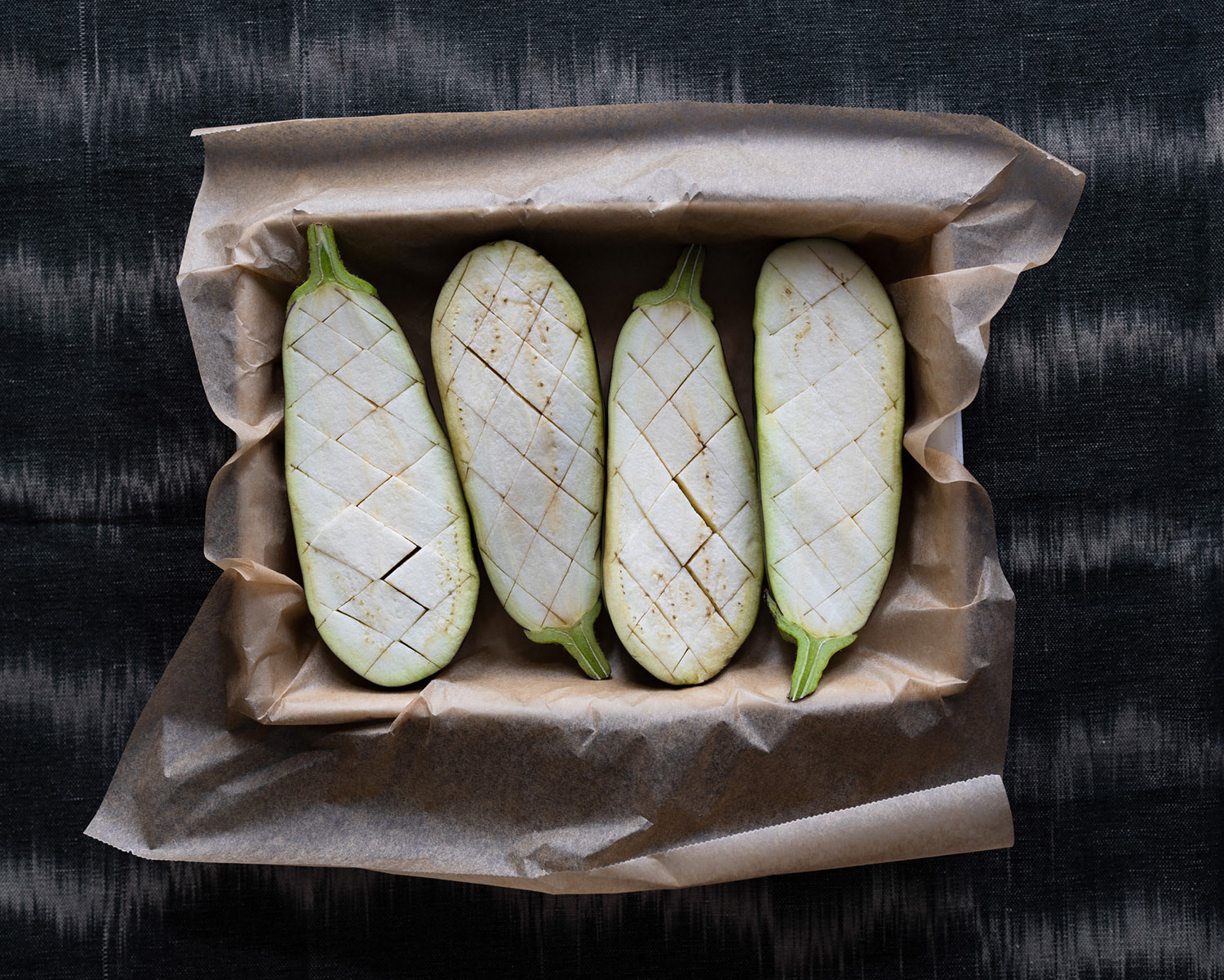 Four eggplant halves arranged in a baking dish lined with baking sheets.