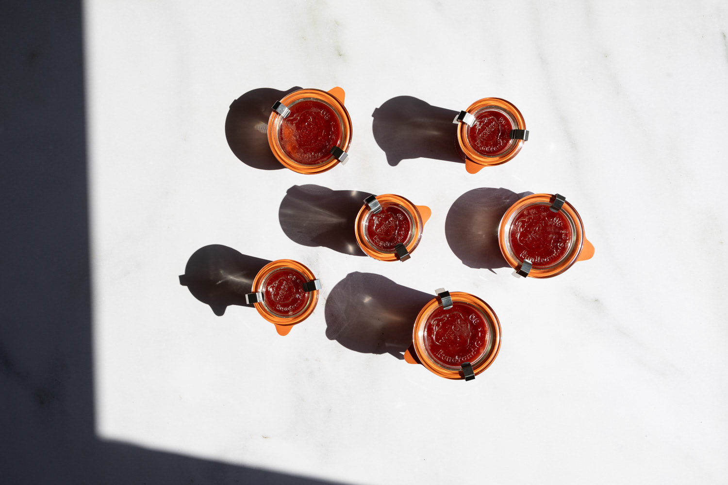 Jars of freshly made strawberry jam seen from above casting shadow in sunlight.