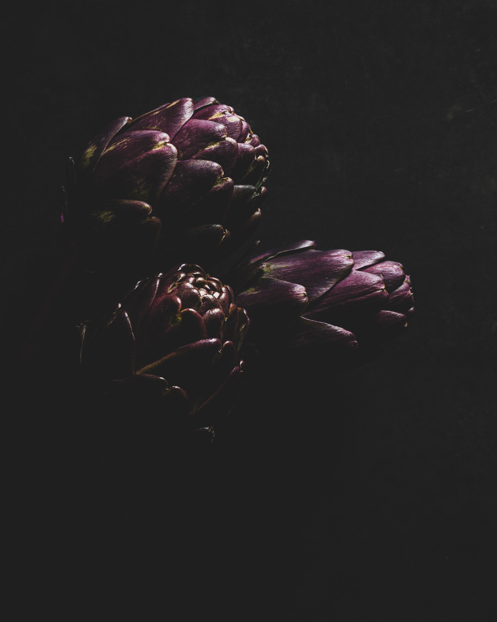Thre artichokes illuminated and partially hidden in black.