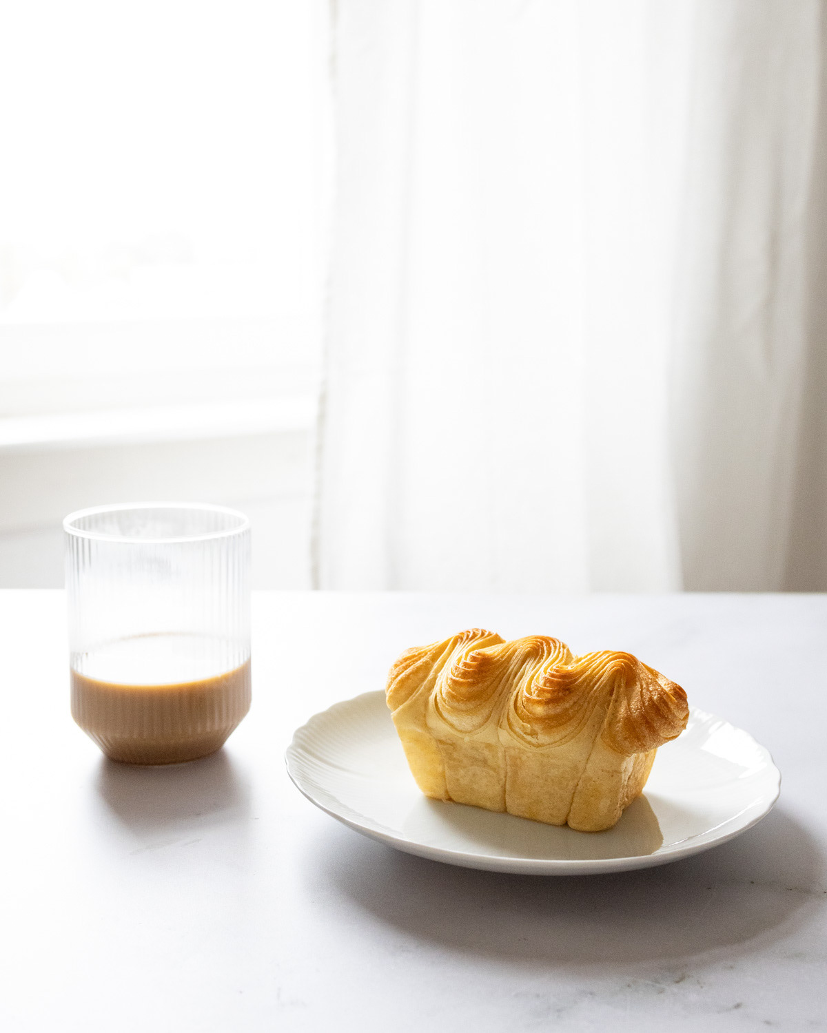Brioche on a white plate with a glass of oat milk coffee.