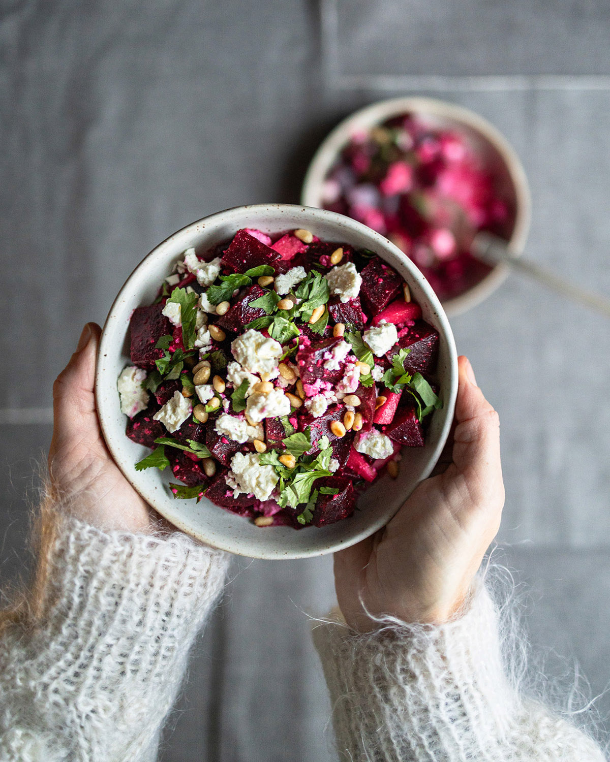 Woman with wool jumper holding a bowl of beetroot salad with feta, pine nuts and fresh coriander.