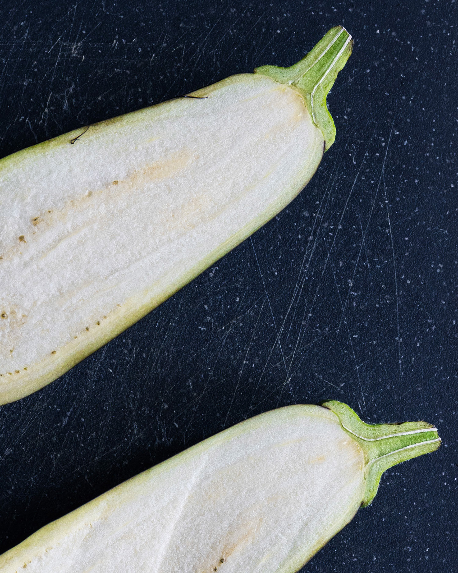 Close up of two aubergine halves on a dark grey cutting board.