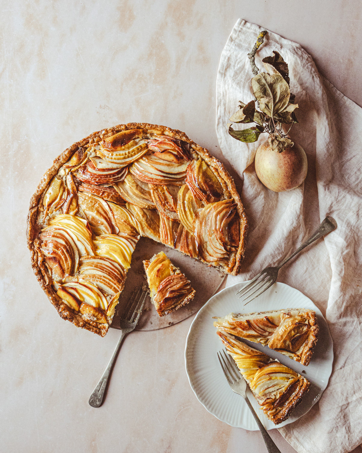 Apple tart with several pieces cut off on a plate with fork and napkin. 