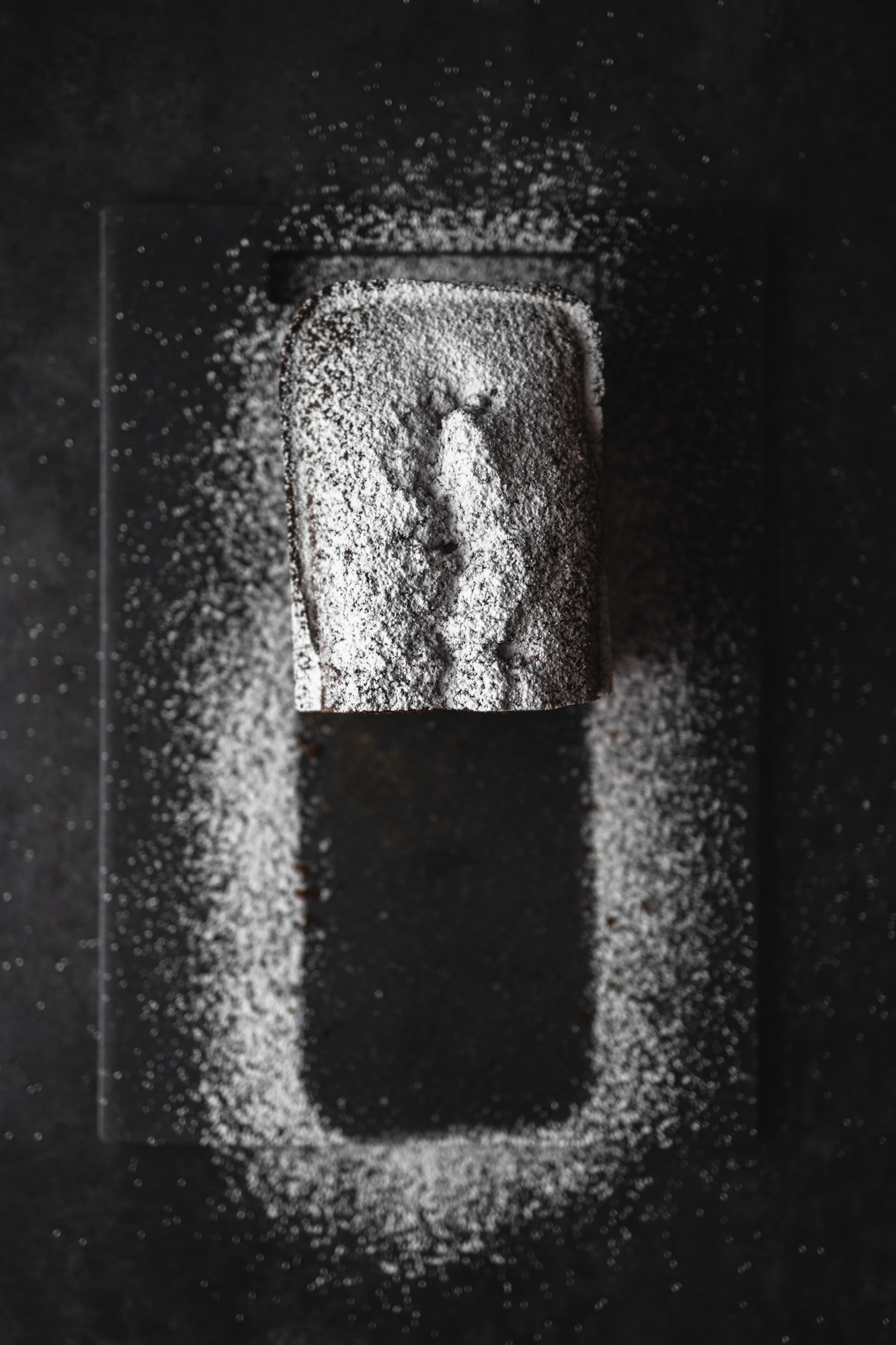 View from top on a cake covered in icing sugar. Part of the cake has been removed, leaving an icing sugar outline behind.