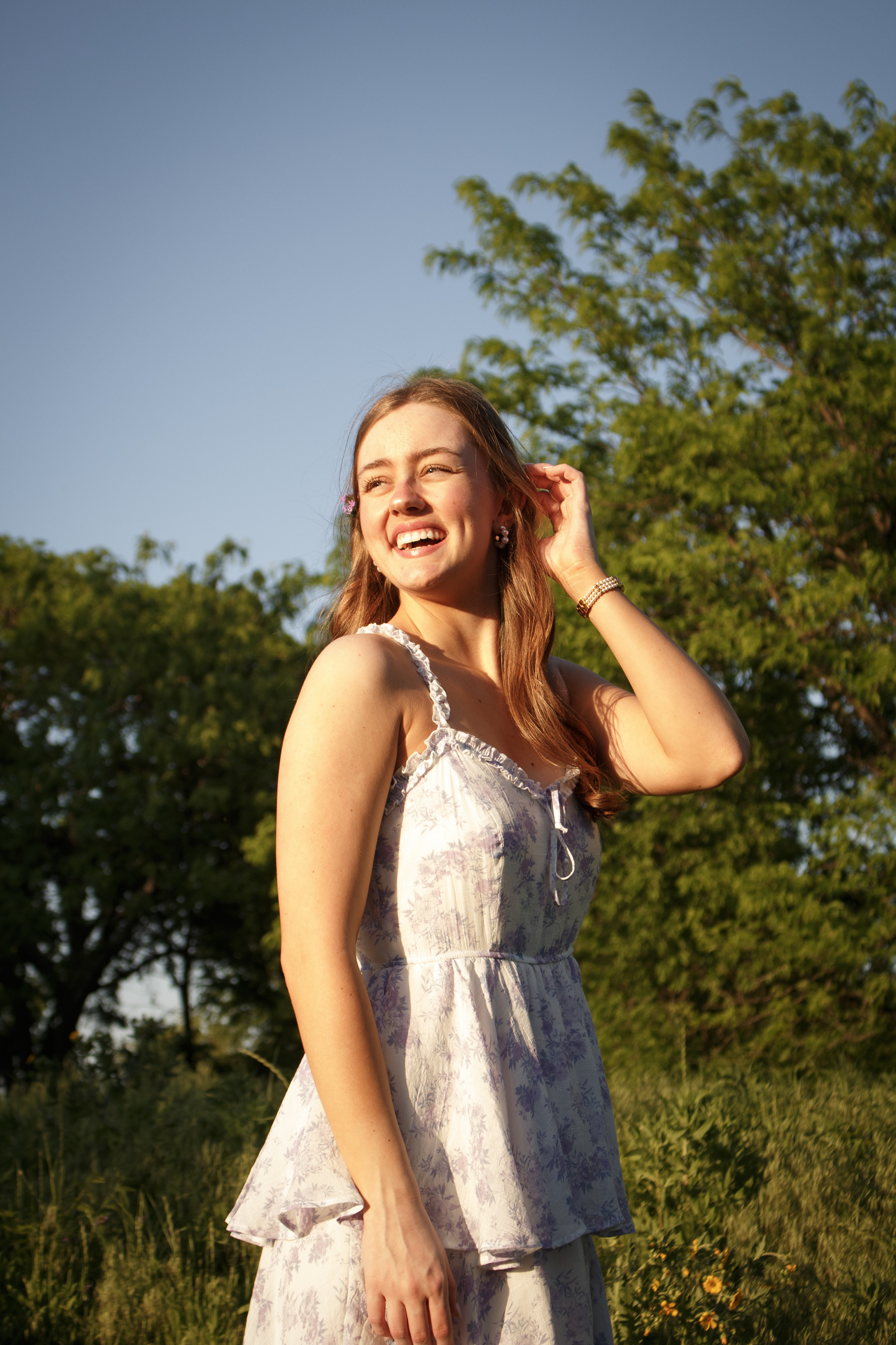 Jade Winn, University of North Texas alumna, laughs and smiles into the sun with a purple flower behind her ear during her portrait session at Arbor Hills Nature Preserve on April 13, 2024. Photo/ Natalie VanDerWal