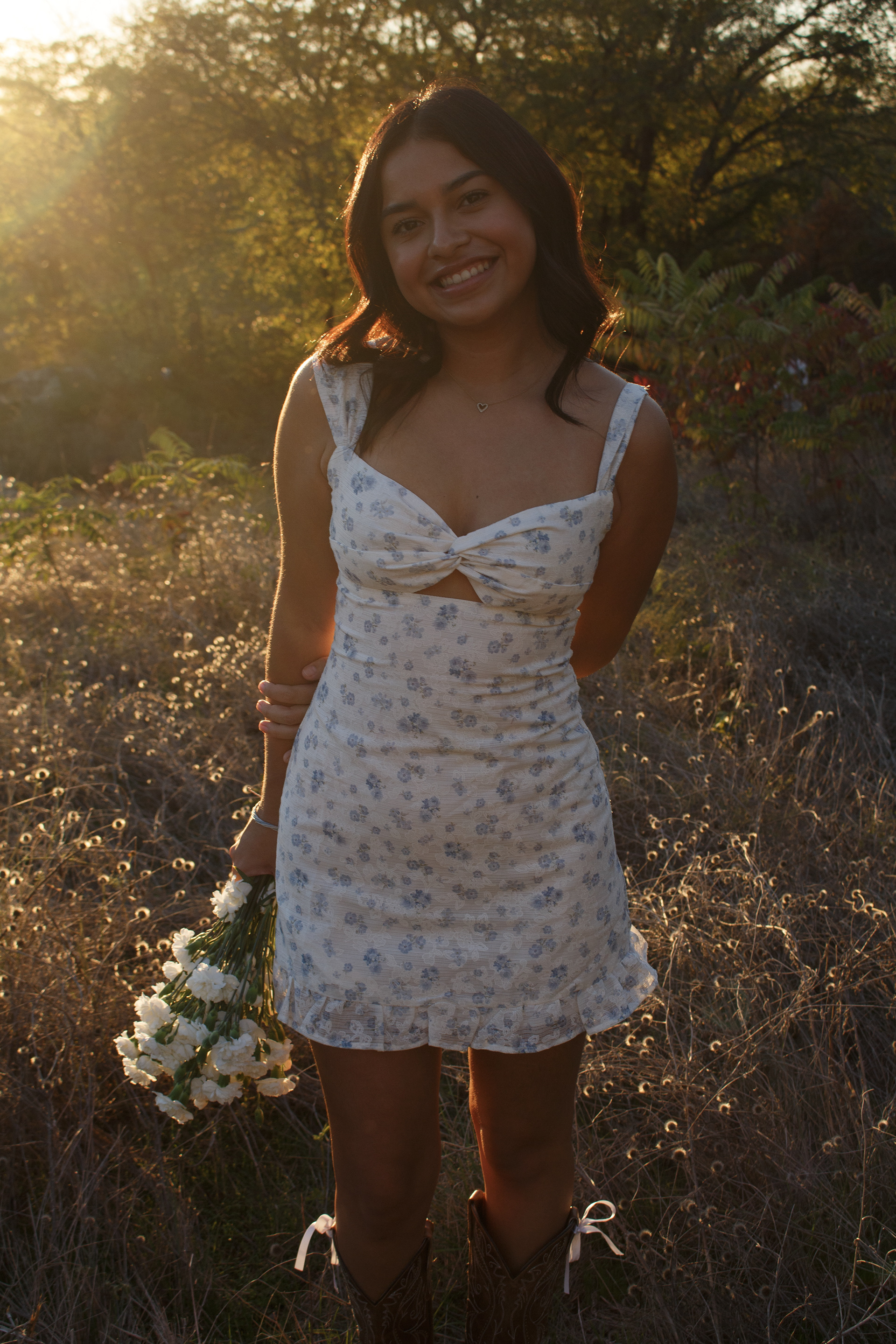 With her arms held behind her back and her bouquet at her side, Gabriela Alaniz smiles at Arbor Hills Nature Preserve on Nov. 10, 2024. Alaniz is immeasurably excited to graduate in May. Photo/ Natalie VanDerWal