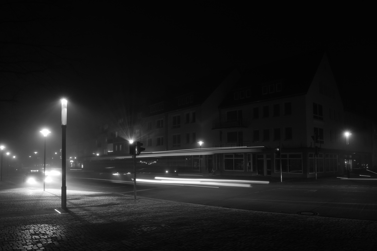 Black and white photograph by Mark Robert Davey of light trails and traffic lights at night in the city.