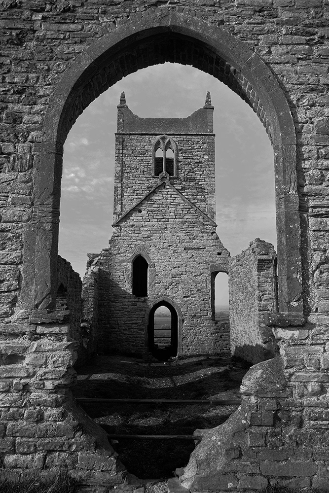 Black and white photograph of the ruins of the church seen through an arch called Burrow Mump, England