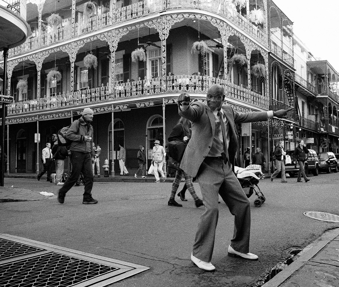 Black and white photograph of a dancing man in a suit and white shoes on the street in New Orleans, USA.
