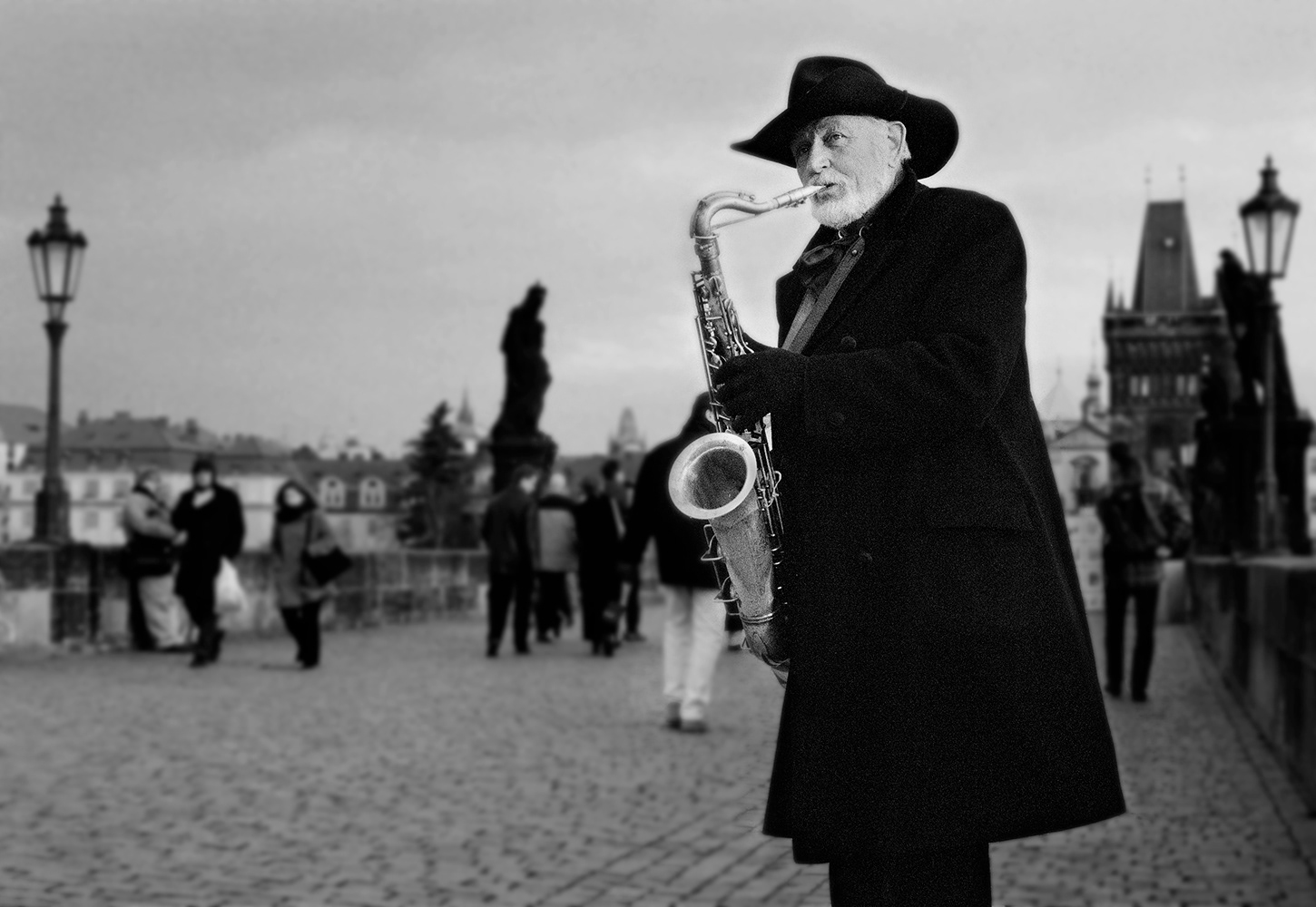 Black and white photograph of a street busker playing a saxophone on St Charles Bridge, Prague, Czech Republic.