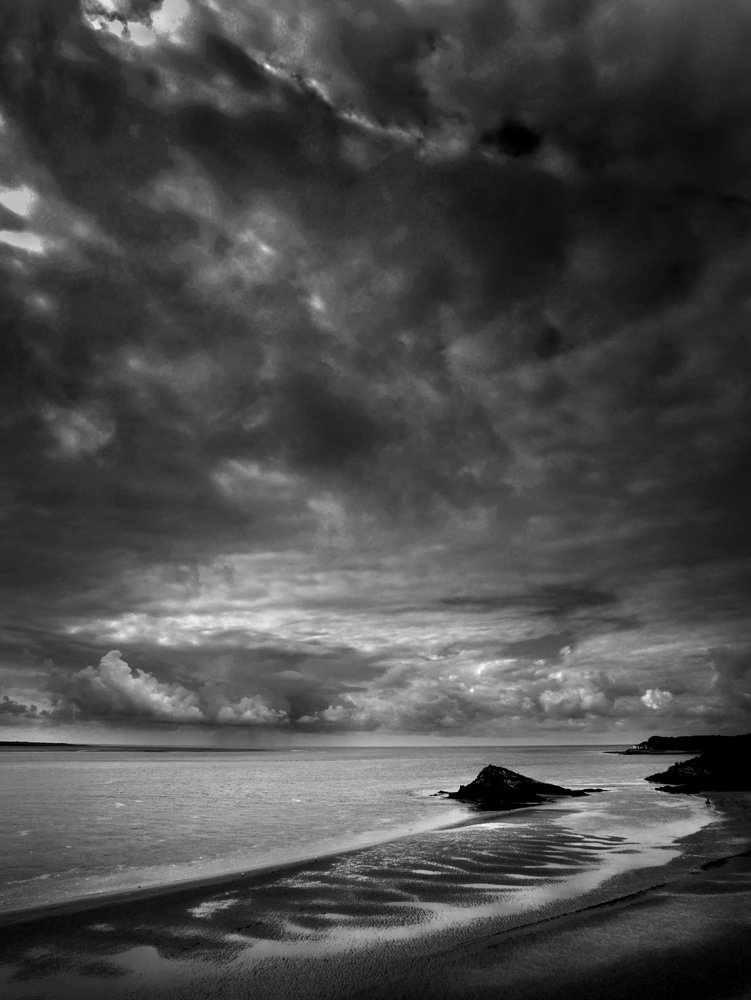Black and white photograph of a storm brewing out at sea with beach in the foreground.