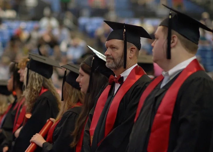 Money at graduation ceremony wearing grad cap and gown with red stole and red bowtie.