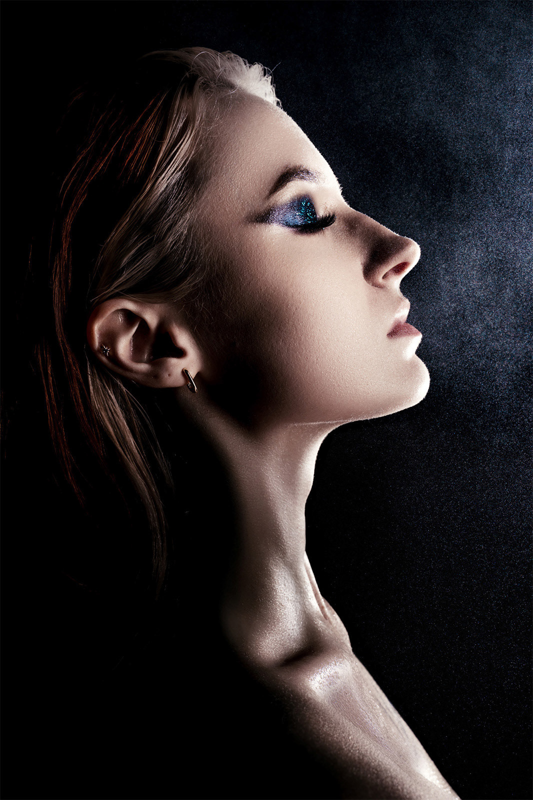 Profilowe ujęcie kobiety z błyszczącym niebieskim makijażem oka, fotografia beauty w stylu fine-art.