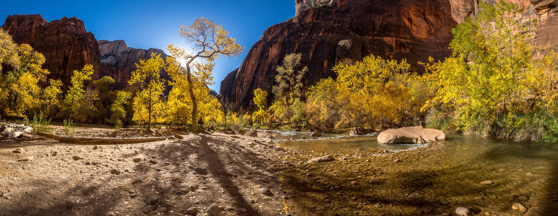 Majestic sandstone cliffs tower over the Virgin River, surrounded by vibrant autumn foliage, inviting relaxation and exploration in Springdale, Utah.