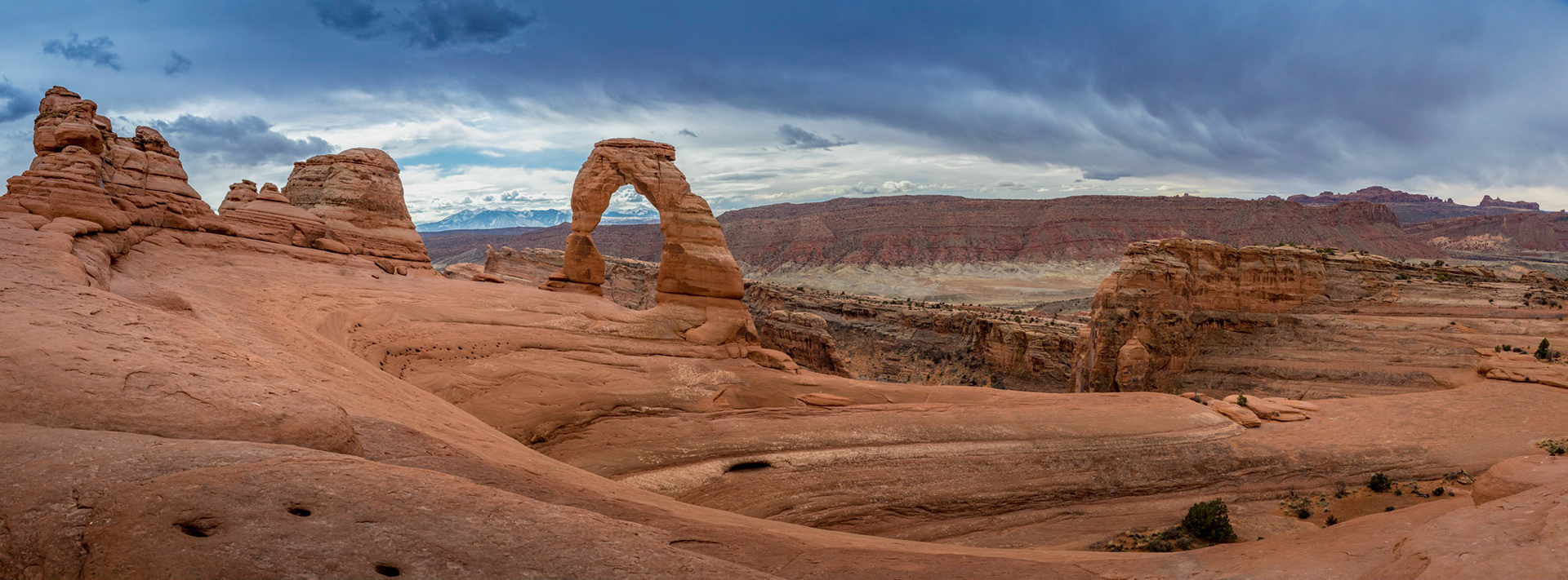 Iconic Delicate Arch landmark standing tall in the Arches National Park on a cloudy day with La Sal Mountains in the background, Moab, Utah