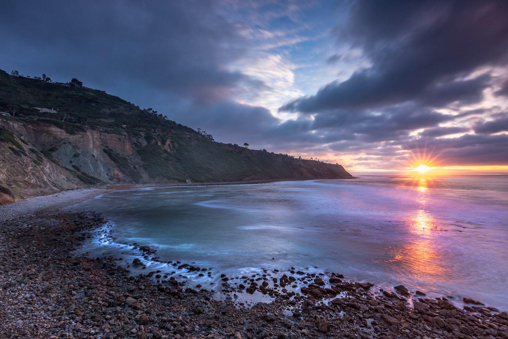 Embark on a serene journey along Bluff Trail, Palos Verdes, Estate, where the sun dips below Bluff Cove, illuminating rugged cliffs and serene ocean waves, creating a tranquil coastal landscape.